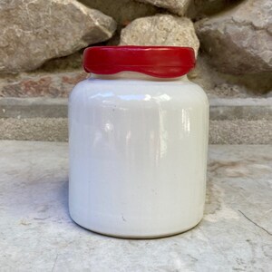 Op de afbeelding: Witte keramische pot met een rood deksel. De pot heeft een gladde, glanzende afwerking.