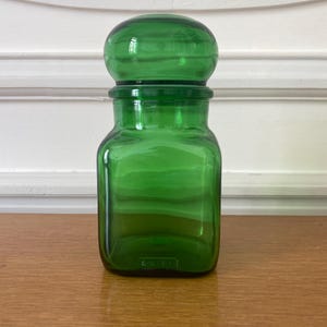 Peut inclure: Un bocal en verre vert vif avec un couvercle rond assorti. Le bocal a une base carrée et un corps cylindrique. Le couvercle est posé sur le bocal, créant un design cohérent. Le bocal est en verre transparent.