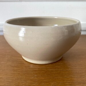 Peut inclure: Un bol en céramique beige de forme ronde avec une finition lisse et brillante. Le bol présente une ouverture large et une base légèrement effilée, affichant une couleur uniforme sur toute la surface extérieure et intérieure du récipient.