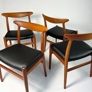 May include: Set of four mid-century modern dining chairs with teak wood frames and black leather upholstery. The chairs have a distinctive curved back design.