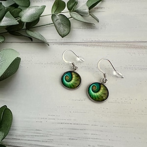May include: A pair of drop earrings featuring circular cabochons with a vibrant green and teal spiral nautilus shell pattern. The earrings are set in silver-toned metal frames and include silver-toned fishhook wires with clear plastic backings.