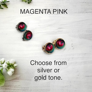May include: Two pairs of round stud earrings featuring a magenta pink and teal spiral pattern. One pair is set in a silver tone metal and the other pair is set in a gold tone metal. The text MAGENTA PINK and Choose from silver or gold tone appear.