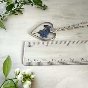 May include: A silver heart-shaped pendant necklace with a clear resin insert containing pressed blue forget-me-not flowers. The pendant is approximately 1 inch in diameter and hangs from a silver chain.