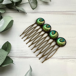 May include: A bronze hair comb with five green and gold spiral patterned cabochons. The comb has a decorative, ornate design.