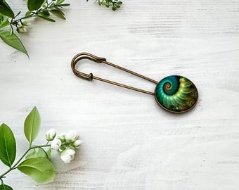 May include: A bronze-toned metal safety pin featuring a circular cabochon setting. The cabochon displays a vibrant, swirling spiral pattern in shades of deep teal, emerald green, and golden yellow, resembling a nautilus shell.