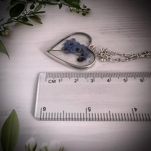 May include: A silver heart-shaped pendant necklace with a clear resin insert containing pressed blue flowers. The pendant is approximately 3 cm wide and is attached to a silver chain.