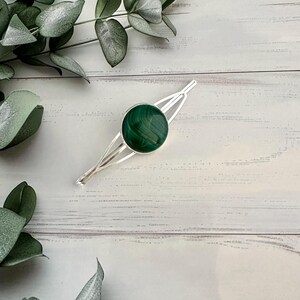 May include: A silver hair clip with a round green malachite stone.
