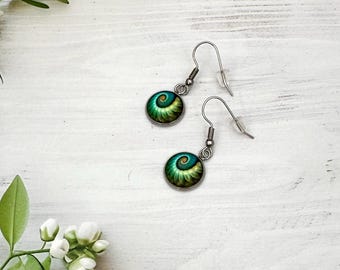 May include: A pair of dangle earrings featuring circular charms with a vibrant teal and lime green spiral pattern. The charms are set in silver-toned metal frames and hang from simple silver-toned ear wires with clear plastic backings.