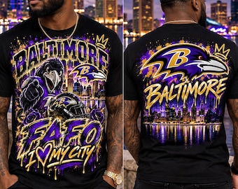 May include: A black t-shirt featuring a graphic print of a raven, a football helmet, and the Baltimore skyline in purple and gold. The text reads BALTIMORE, FAFO, I LOVE MY CITY, and RAVENS NATION. The design includes paint splatter effects.