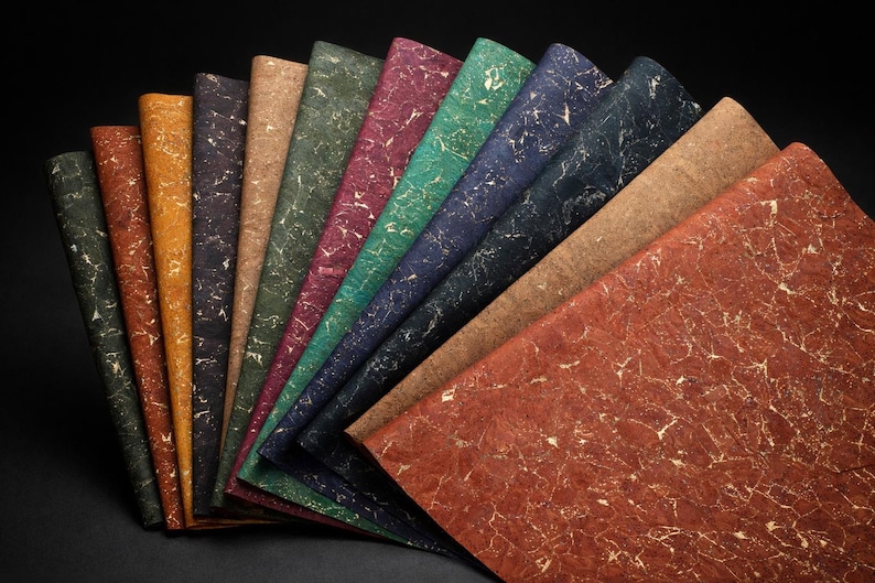 May include: A collection of textured paper sheets in various colors, including green, brown, and red, arranged in a fan shape. Each sheet has a unique pattern of gold-colored veins, creating a marbled effect. The background is black.
