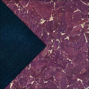 May include: A sheet of purple cork fabric with a natural, irregular cracked texture and gold-colored metallic flecks throughout, layered over a solid dark navy blue fabric with a smooth, matte, and slightly fuzzy textile surface.
