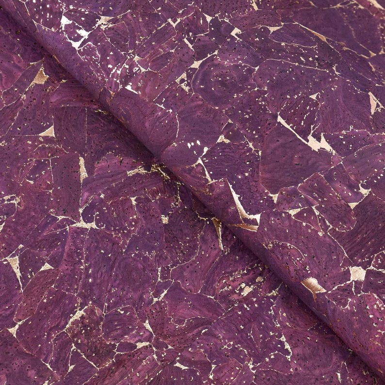 May include: Close-up of a roll of purple cork fabric with gold metallic accents. The cork has a mosaic-like pattern with irregular shapes and a textured surface. The gold leaf adds a touch of luxury to the design.