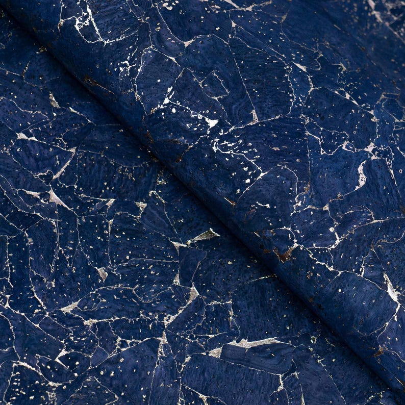 May include: Close-up of a navy blue cork fabric with a silver metallic veining pattern. The fabric is folded, revealing the texture and color variations. The design resembles a marble or stone effect.