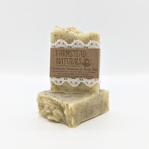 Puede incluir: Dos barras de champú y jabón corporal hechos a mano apiladas una encima de la otra. La barra superior tiene una etiqueta marrón que dice "FARMSTEAD NATURALS HANDCRAFTED IN DEPOCHE, B.C. Handmade Shampoo & Body Bar Sustainable Palm oil, Coconut oil, Castor oil, Cocoa Butter, Nettle Leaf, Essentials oils of Peppermint, Eucalyptus, Rosemary, Lavender, Tea Tree & Lemon".