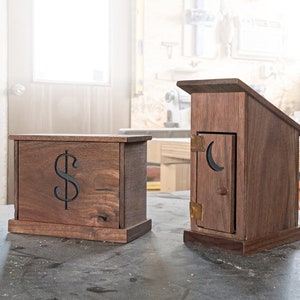 May include: Two wooden boxes, one with a dollar sign carved into the front and the other shaped like an outhouse with a crescent moon cutout.