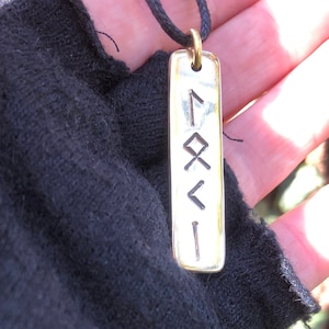 May include: A silver pendant with a black cord necklace. The pendant is rectangular and has four runes engraved on it.