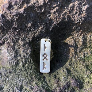 May include: A silver charm with four runes engraved on it. The runes are "F", "U", "Th", and "R".