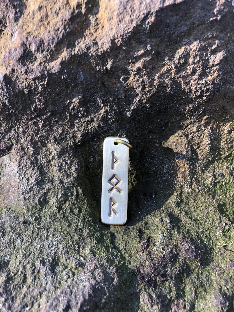 May include: A silver charm with four runes engraved on it. The runes are "F", "U", "Th", and "R".