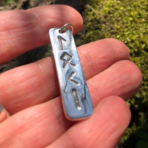 May include: Silver pendant with a vertical row of five runes engraved on it. The runes are in a simple, modern style.