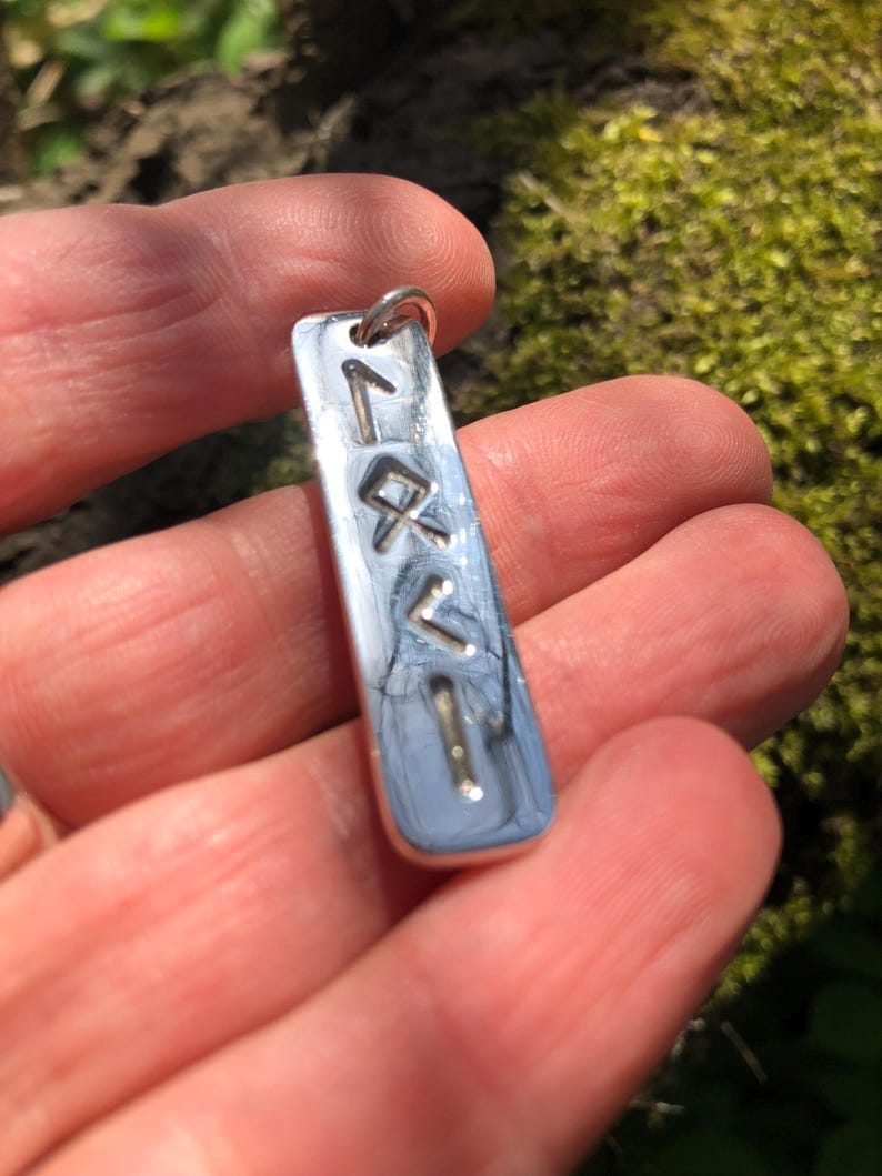 May include: Silver pendant with a vertical row of five runes engraved on it. The runes are in a simple, modern style.