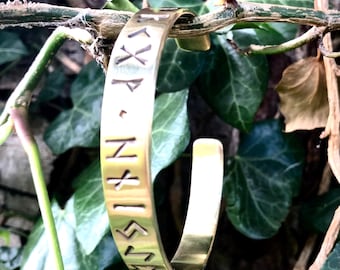 May include: A gold-colored metal bracelet with a series of runes engraved on the surface.