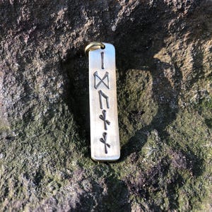 May include: A silver metal keychain with a vertical row of five Norse runes engraved on it. The runes are: Isa, Nauthiz, Jera, Ansuz, and Dagaz.