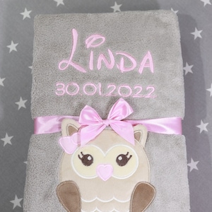 Könnte beinhalten: Eine graue Babydecke mit einem rosa Eulen-Applikationen und einem rosa Band. Die Decke ist mit dem Namen "Linda" und dem Datum "30.01.2022" bestickt.