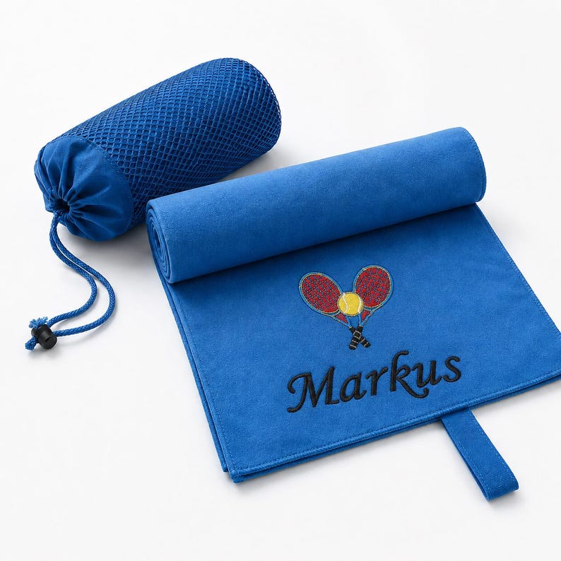 Op de afbeelding: Een koningsblauwe microvezel handdoek met een geborduurd ontwerp van twee gekruiste tennisrackets en een gele tennisbal, met de naam Markus in zwarte draad eronder gestikt. De handdoek bevat een bijpassende blauwe mesh tas met trekkoord.