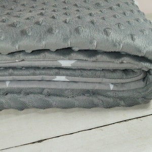 Op de afbeelding: Een grijze en witte babydeken met een zachte, pluche textuur. De deken is dubbelgevouwen en heeft een subtiel sterrenpatroon.