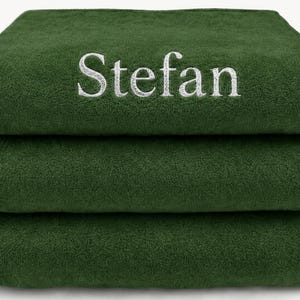 Op de afbeelding: Een stapel van drie gevouwen donkerbosgroene handdoeken. De bovenste handdoek is voorzien van de naam Stefan, geborduurd in wit garen in een schreeflettertype. De handdoeken hebben een zachte, pluche textuur en zijn netjes op elkaar gestapeld.