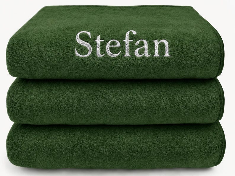 Op de afbeelding: Een stapel van drie gevouwen donkerbosgroene handdoeken. De bovenste handdoek is voorzien van de naam Stefan, geborduurd in wit garen in een schreeflettertype. De handdoeken hebben een zachte, pluche textuur en zijn netjes op elkaar gestapeld.