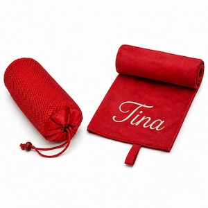 Op de afbeelding: Een rode microvezel handdoek met de naam Tina geborduurd in wit schrift, voorzien van een ophanglus, naast een bijpassende rode mesh opbergtas met trekkoord, beide items gepresenteerd op een effen witte achtergrond.