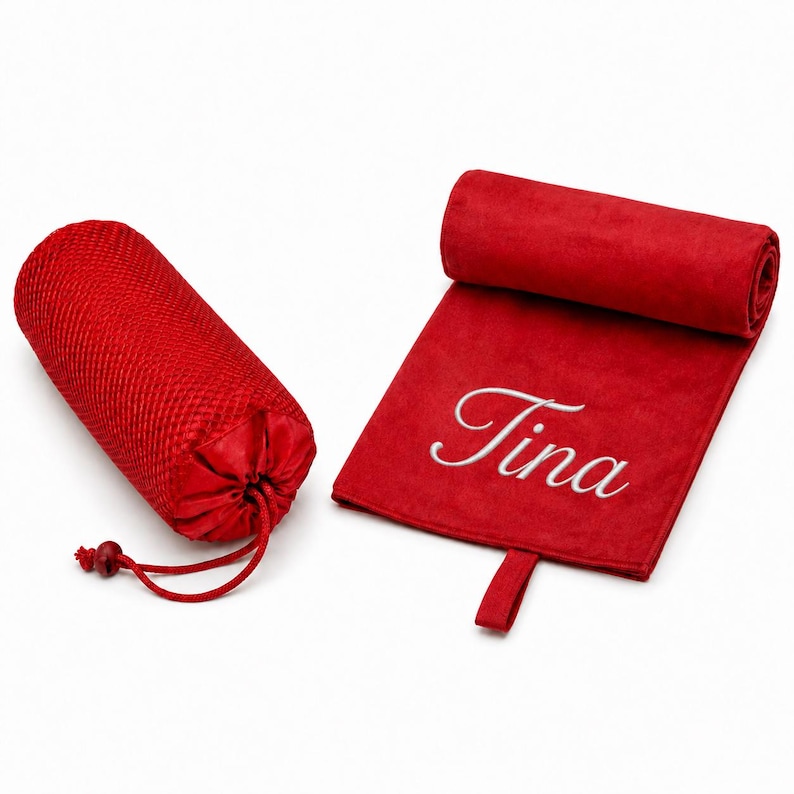 Op de afbeelding: Een rode microvezel handdoek met de naam Tina geborduurd in wit schrift, voorzien van een ophanglus, naast een bijpassende rode mesh opbergtas met trekkoord, beide items gepresenteerd op een effen witte achtergrond.