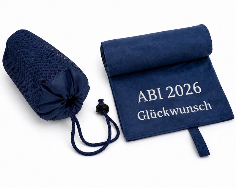 Op de afbeelding: Een marineblauwe microvezel handdoek met de witte geborduurde tekst ABI 2026 Gl&uuml;ckwunsch, vergezeld door een bijpassende marineblauwe mesh opbergtas met trekkoordsluiting, gepresenteerd tegen een effen witte achtergrond.