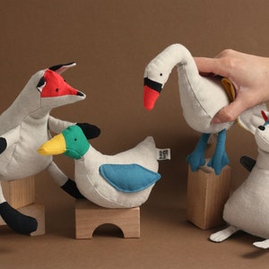 May include: Four plush stuffed animals: a fox with a red tail, a duck with a green head and blue wings, a swan with a red beak, and a raccoon with a blue face and striped tail.