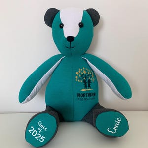 May include: A teal green teddy bear with white accents and black ears. The bear has a logo embroidered on its chest that says "Northern Federation" and a tree with two children standing under it. The bear's left foot has "Class of 2025" embroidered on it and the right foot has "Ernie" embroidered on it.