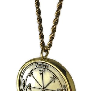 May include: A gold chain necklace with a round pendant featuring a silver seal with a star and symbols in the center. The pendant has a gold rim and the text "Iebvbay" is inscribed on the top.