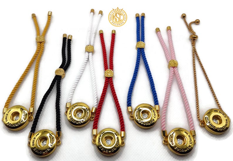 May include: A collection of adjustable bracelets with gold-colored metal accents and colorful rope cords. Each bracelet features a round, gold-colored charm with the text "KING SOLOMON COIN". The cords are in various colors, including yellow, black, white, red, blue, pink, and gold.