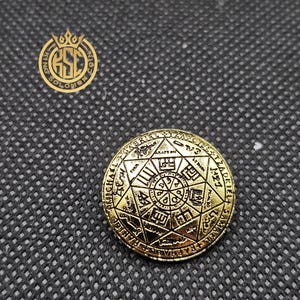 May include: A gold-colored coin with intricate engravings of symbols and text. The coin features a central design surrounded by a circular border with inscriptions. The coin is set against a dark, textured background, with the words "KING SOLOMON COIN" in a logo.