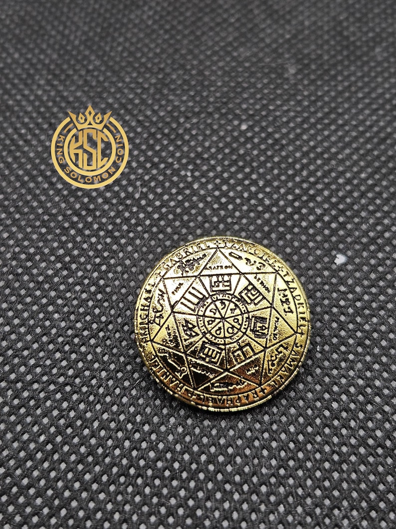 May include: A gold-colored coin with intricate engravings of symbols and text. The coin features a central design surrounded by a circular border with inscriptions. The coin is set against a dark, textured background, with the words "KING SOLOMON COIN" in a logo.