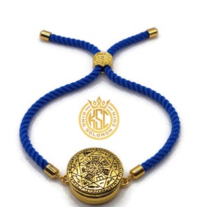 May include: A gold-colored bracelet with a circular pendant featuring intricate engravings. The bracelet has a blue rope-like band with gold-colored accents. The pendant has a detailed design with symbols and text. The bracelet is adjustable.