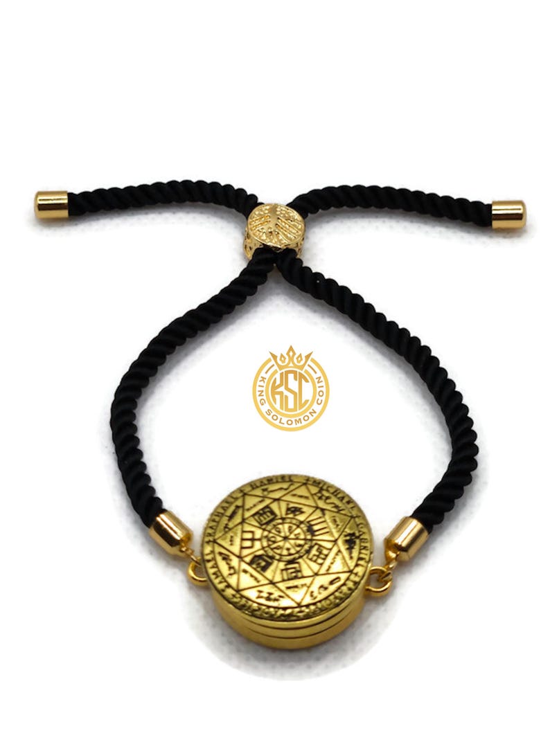 May include: Gold-colored bracelet with a circular pendant featuring an engraved design and black rope-like cord. The bracelet has gold-colored end caps and a gold-colored adjustable clasp. The pendant has the text "KING SOLOMON" on it.