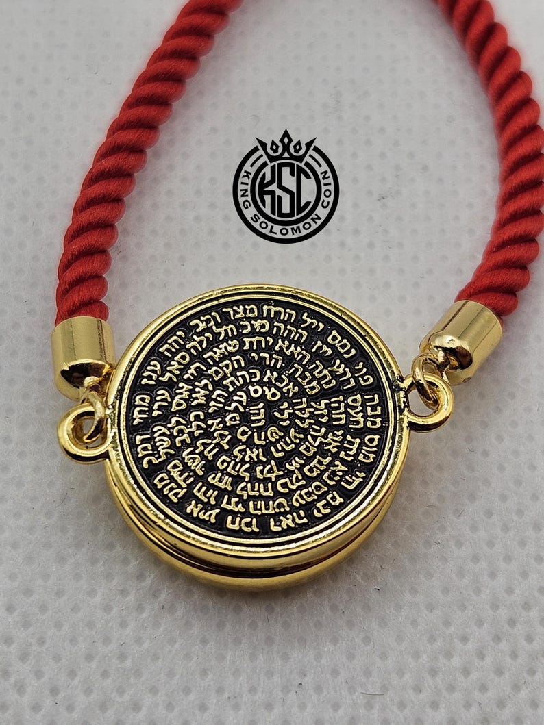 May include: A gold-colored pendant with black text, attached to a red rope bracelet. The pendant has a circular design with Hebrew text. The bracelet has gold-colored clasps. The logo "KING SOLOMON COIN" is visible.