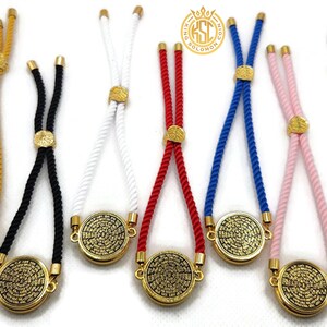 May include: A collection of adjustable bracelets in various colors, including gold, black, white, red, blue, and pink. Each bracelet features a gold-colored circular pendant with an intricate design and a sliding knot closure.
