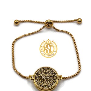 May include: Gold-toned adjustable bracelet featuring a circular pendant with intricate black text. The pendant is the focal point, connected to a delicate chain with a sliding bead closure. The bracelet has a logo that says "King Solomon Coin".