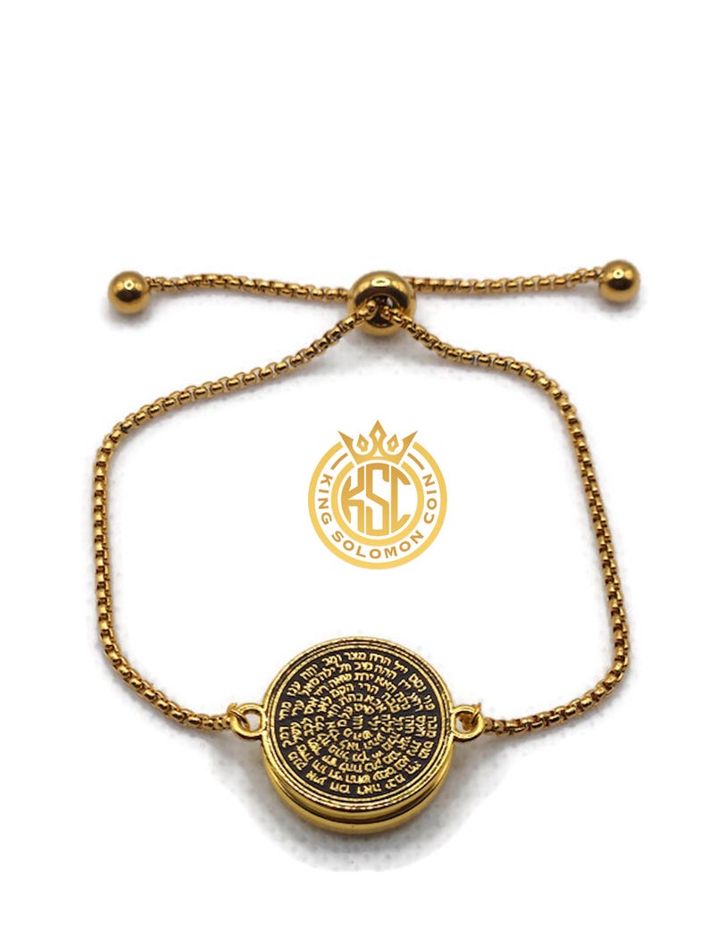 May include: Gold-toned adjustable bracelet featuring a circular pendant with intricate black text. The pendant is the focal point, connected to a delicate chain with a sliding bead closure. The bracelet has a logo that says "King Solomon Coin".