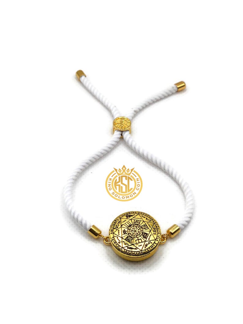 May include: A gold-colored bracelet with a circular pendant featuring intricate designs. The pendant is connected to a white rope-like band with gold-colored accents. The bracelet is adjustable and has a logo that says "King Solomon Coin".