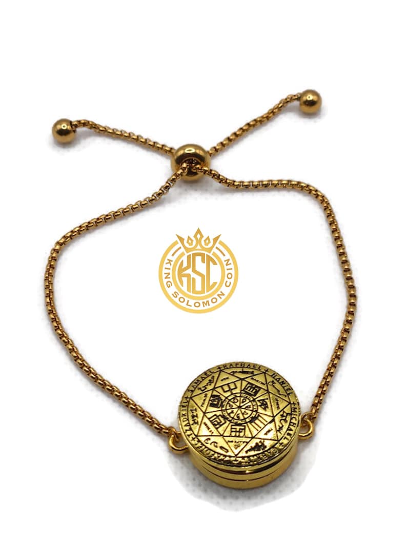 May include: Gold-toned adjustable bracelet featuring a circular pendant with intricate engraved symbols and text. The pendant is the focal point, connected to a delicate chain with a sliding bead for adjustment. The bracelet has a polished finish.
