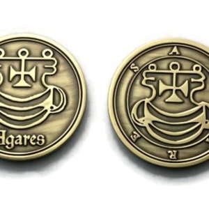 May include: Two gold-colored metal coins with a design of a cross and a symbol. The coin on the left has the word "Agares" inscribed on it. The coin on the right has the letter "A" at the top and the letter "R" at the bottom.