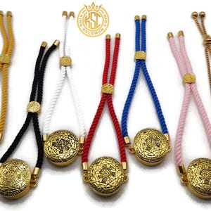 May include: An assortment of adjustable bracelets with gold-colored circular pendants and rope or chain straps in various colors, including yellow, black, white, red, blue, and pink. The pendants have an intricate design.
